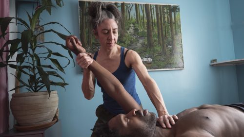 Éliane massant un homme couché sur table de massage, manoeuvre de mobilisation du bras